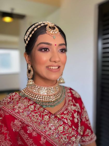 A classic morning bride look in a red lehenga, featuring a sleek hairstyle with a matha patti and subtle, glowing makeup.