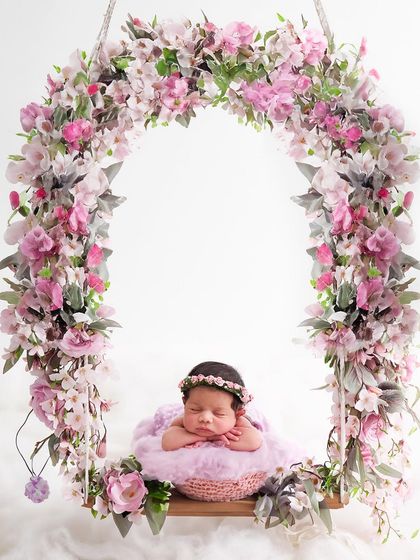 This sleeping newborn is framed by a beautiful arch of pink flowers while resting on a swing, creating a breathtaking and whimsical floral portrait.