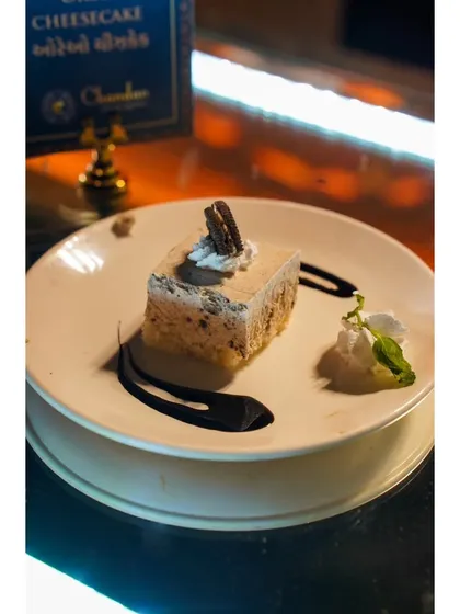 An Oreo Cheesecake slice, perfectly plated with a swirl of chocolate sauce. A modern classic that is always a crowd-pleaser.