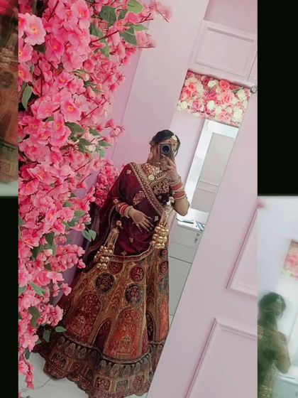 A mirror selfie capturing the full glory of a maroon and mustard bridal lehenga, set against a wall of pink flowers. This shows the outfit in a modern, personal context.