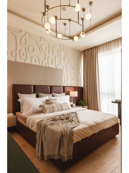 The bedroom area features a tan leather headboard set against a fluted panel and a custom Art Deco-inspired wall relief. This layered backdrop adds texture and visual interest, serving as the room's focal point.