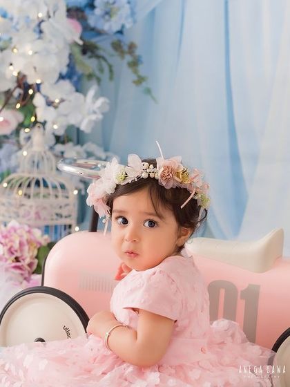 A sweet glance over her shoulder. The baby girl sits in a pink toy car that perfectly matches her dress and the floral theme.