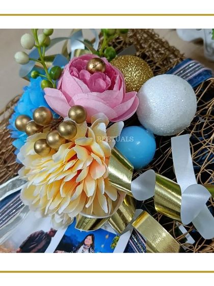 A beautiful floral arrangement with blue, pink, and yellow flowers, used as a decorative topper for a wedding hamper.