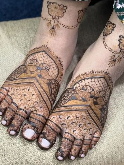 This foot mehandi features graceful peacock motifs with detailed check patterns. The design extends to a delicate vine on the ankle, resembling a beautiful piece of jewelry.