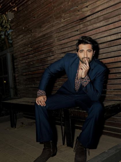 A full-length seated portrait from the same series, using the rustic wooden bench and wall as a textured backdrop.