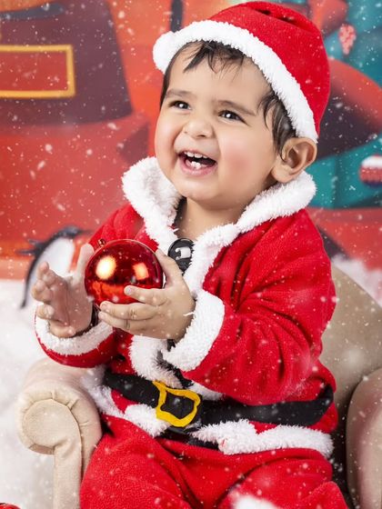 A big, bright smile from this baby Santa, holding a shiny red ornament.