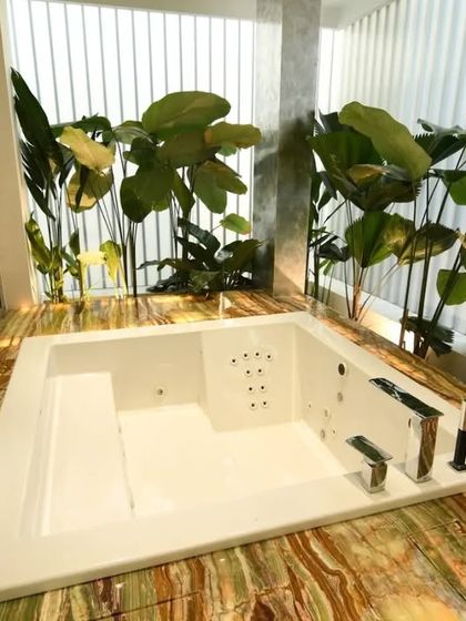 A luxurious jacuzzi tub set in a bed of green and gold onyx-style marble, surrounded by lush indoor plants. This design blurs the line between a bathroom and a tropical spa retreat.