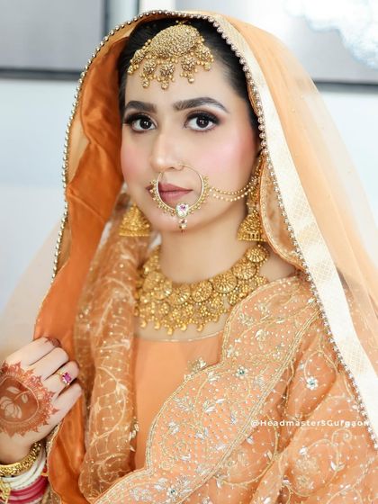 A beautiful Sikh bride in a peach-colored suit. The makeup is soft and radiant, with a focus on her eyes, and the look is completed with a traditional nath and maang tikka.