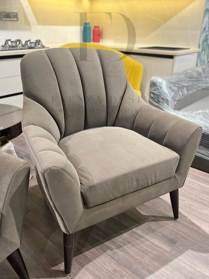 A pair of armchairs in a muted grey fabric with a fan-like, channel-tufted back. The design is subtle yet sophisticated, offering a modern take on a classic silhouette.
