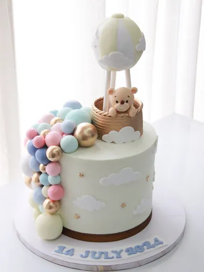 A whimsical hot air balloon cake to welcome a new baby, featuring a cascade of pastel balloons in pink, blue, and gold.