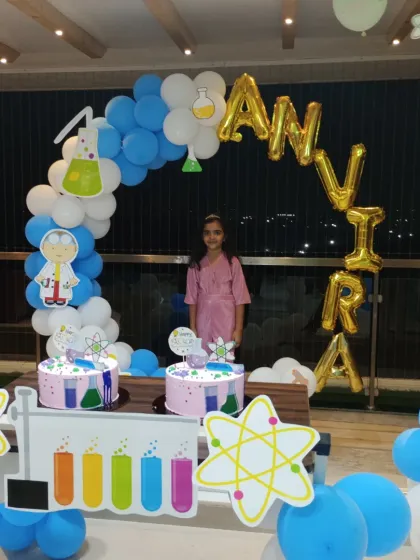 A unique Science theme party for a curious mind. This decoration features a custom balloon arch with science-themed cutouts like beakers and atoms, two themed cakes, and a personalized name banner.
