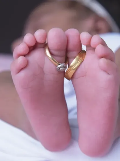 A close-up shot focusing on the baby's tiny feet, adorned with the parents' wedding rings. This is a classic and powerful newborn photo that symbolizes the start of a new family journey.