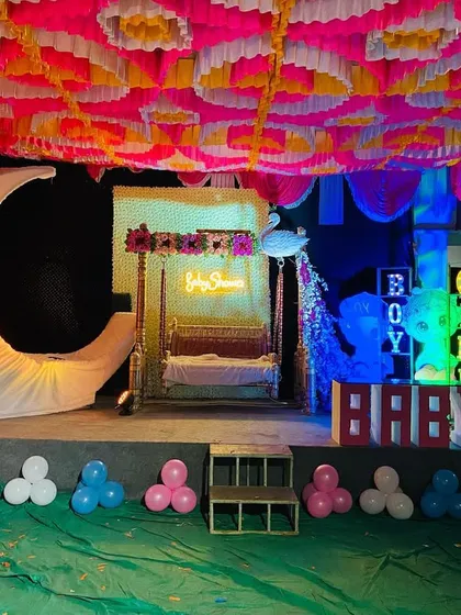 A baby shower stage with a large moon prop and a decorated swing under a colorful pandal.