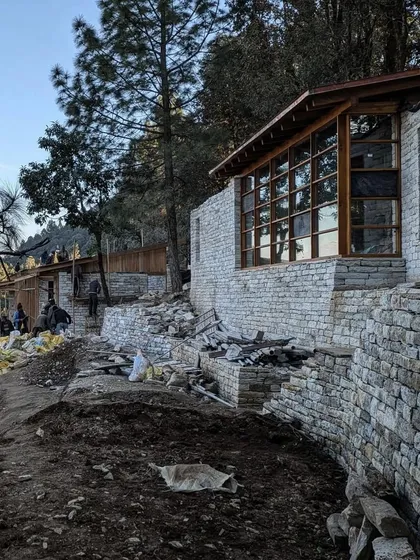 An exterior view of the main lodge building under construction. The long, low profile of the structure follows the curve of the hillside, and the use of local stone helps to ground it firmly in its environment.