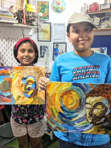 A collaborative spirit in the studio. Two students proudly display their expressive Buddha paintings, each with a unique and colorful style.