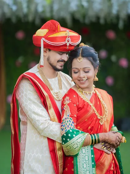 A beautiful portrait of a Maharashtrian couple, with the bride in a classic red and green Paithani saree and the groom in a matching red pheta.