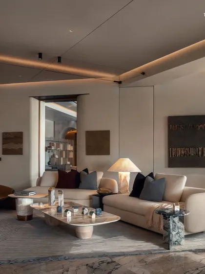 The living room at Palais Royale, where a sculptural coffee table and curved sofas anchor the room. The design's organic silhouettes add drama, while the soft glow of ambient lighting enhances the subtle veining of the marble flooring.