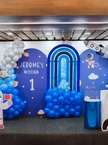 Blast off with a space-themed first birthday party, "Jerome's Mission 1." This out-of-this-world decor includes astronaut and rocket ship cutouts, planet-themed backdrops, and a galaxy of blue and silver balloons to create an exciting cosmic adventure for your little one.