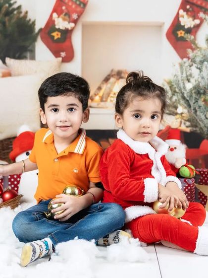 Two siblings sitting in a festive Christmas setup. This photo captures the wonder and excitement of the holiday season for young children.