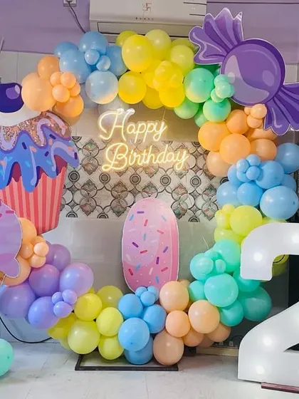 A delicious-looking candyland themed second birthday. The decor features a colorful balloon ring with large cutouts of an ice cream cone, a cupcake, and candy.