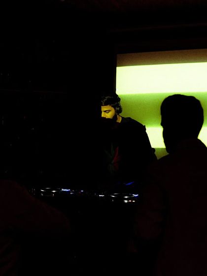 A silhouette against the visuals, a moment of calm before dropping the next track. It's all about building tension and release.