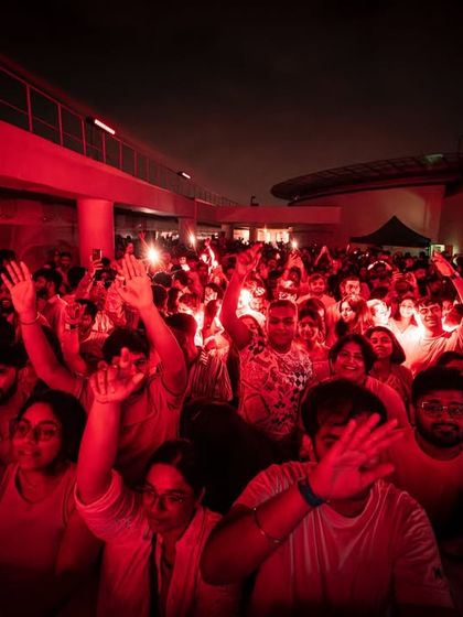 A crowd of partygoers dressed in white, dancing under red lights. The strict all-white dress code creates a visually stunning and unified aesthetic for the event.