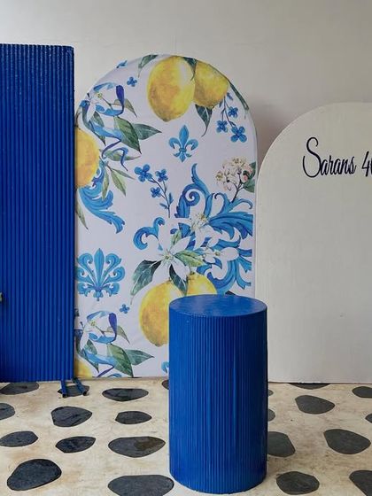 A full view of the Amalfi-themed setup for Saran's 40th birthday. We combined a custom lemon-print arch, a bold blue textured panel, and a personalized white arch with a fun balloon garland.