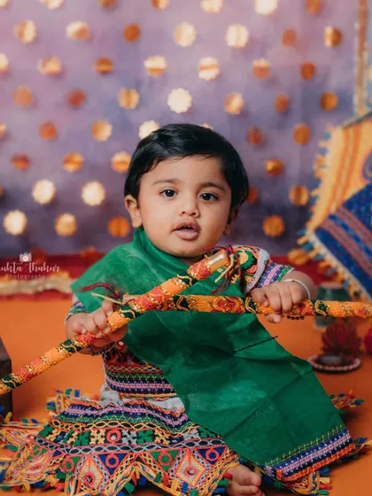 This little Radha is ready to steal the show with her dandiya sticks. The vibrant colors of the Navratri setup make for such joyful photos.