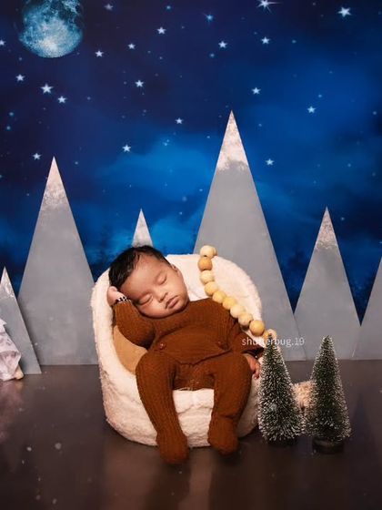 A mountain adventure theme for a 28-day-old baby boy. He sleeps soundly in a comfy chair, surrounded by mountain cutouts, a teepee, and a starry sky.