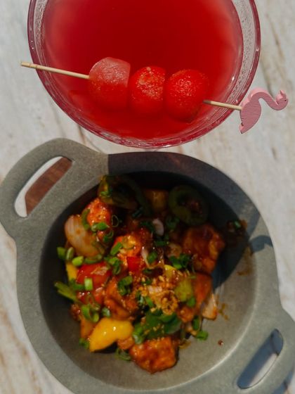 A top-down shot of a vibrant red mocktail and a plate of delicious chili paneer at Camo Noida, highlighting the aesthetic presentation of their food.