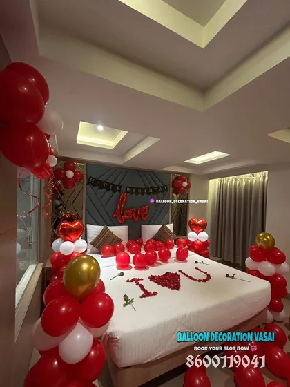 An angled view of a classic red and white romantic room surprise. This shows the balloon columns and how the decorations frame the bed, making it the focal point of the room.
