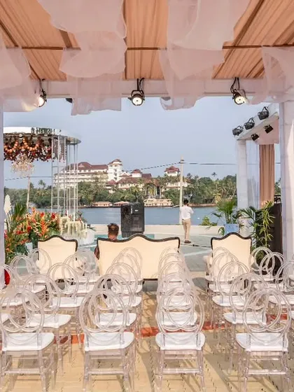 A modern, minimalist ceremony setup overlooking the water. The clean lines of the draped canopy and transparent ghost chairs ensure the stunning view remains the star of the show.