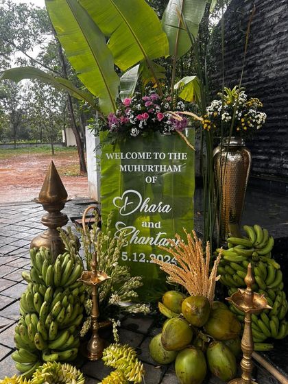A traditional 'Muhurtham' welcome sign made of a translucent green material, surrounded by coconuts, bananas, and brass lamps, perfectly capturing the essence of a South Indian welcome.
