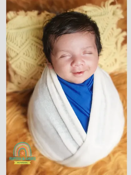 That fleeting, sleepy smile is what we live to capture. This little one, wrapped snugly in white and blue, shows the pure joy of a newborn's dreams.