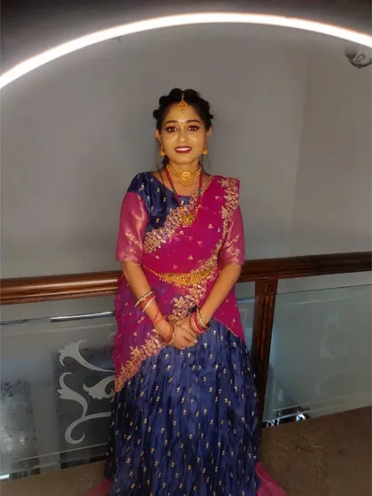 This look is for a half-saree ceremony. The makeup is kept youthful and bright, with pink and gold tones to match her beautiful blue and pink outfit.
