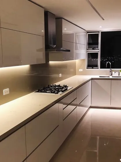 A pristine, all-white modular kitchen with handleless cabinets and warm under-cabinet lighting. This design, part of a larger home project, emphasizes a clean, minimalist aesthetic with a focus on functionality.