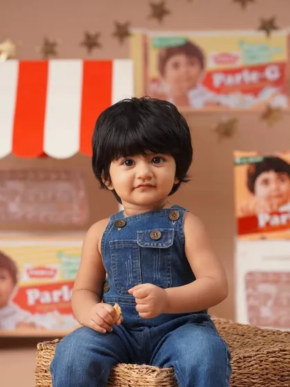 A close-up portrait for a nostalgic Parle-G themed first birthday shoot, with the baby girl in denim overalls looking just like the iconic biscuit brand's mascot.
