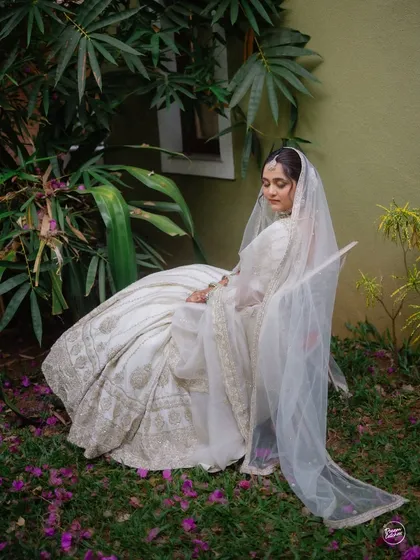 A tranquil portrait of the bride seated in a garden, her white lehenga and veil creating a beautiful contrast with the surrounding greenery.