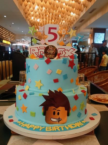 This two-tier Roblox cake is ready for a 5th birthday party. The bright blue cake is decorated with colorful blocks, stars, and a popular character from the game, making it a hit with young gamers.