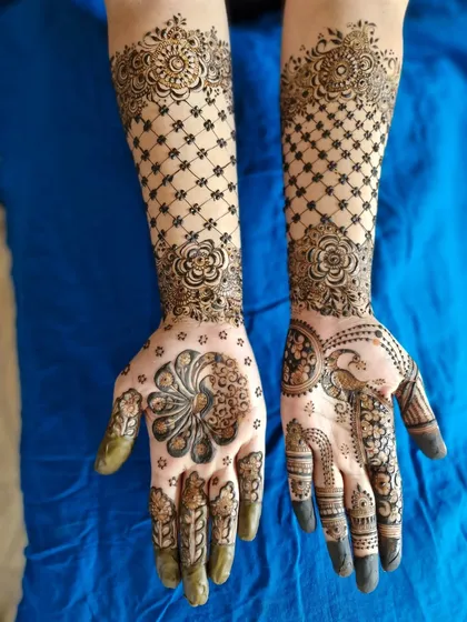 A lovely engagement mehendi in an Indo-Arabic style. It features a large, stylized peacock on one palm and a net pattern on the arms.