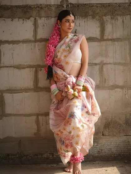 A full-length view of the floral saree look, showing the unique dhoti-style drape. The styling with pastel bangles and a long floral braid creates a fresh, youthful, and rustic aesthetic.