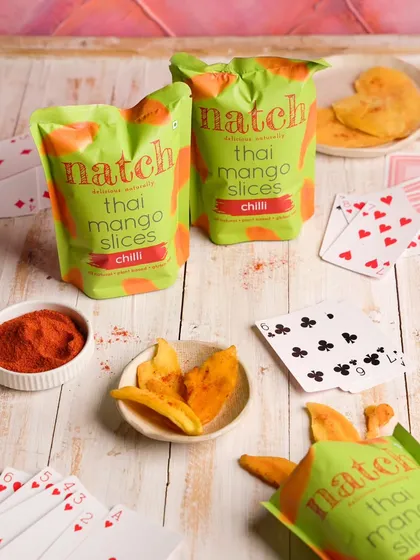 This shot for a brand of Thai mango slices is styled to evoke a fun, casual snack time. The playing cards and chili powder as props suggest a spicy, playful treat to be shared with friends.