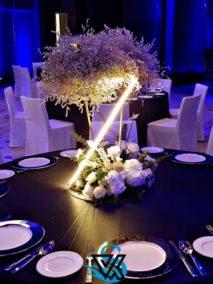 A dining table setup with a striking black tablecloth and blue-rimmed plates. The centerpiece combines natural elements with a modern, illuminated geometric structure, perfectly capturing the event's theme.