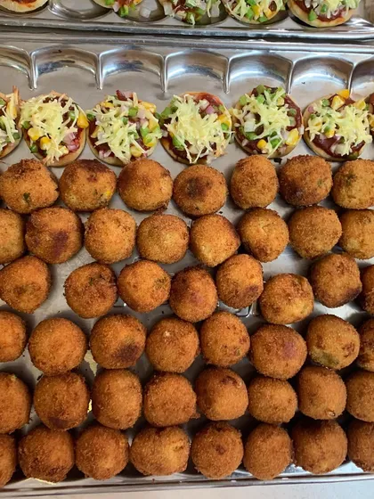 A tray of golden-brown Corn and Cheese Balls lined up next to Mini Veggie Pizzas, ready to be served at a party.