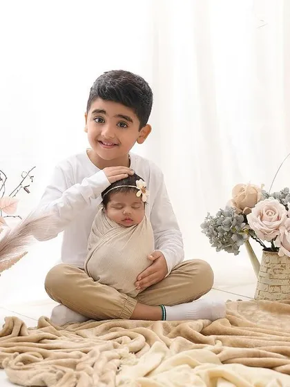 A proud big brother gently holds his newborn sibling. We love capturing these first moments of a new sibling bond in our studio, surrounded by soft, neutral-toned props.