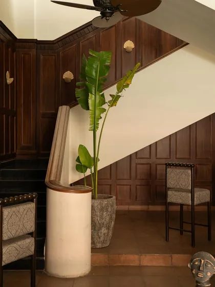 A detail of the staircase, where the dark wood paneling creates a dramatic backdrop for a modern, sculptural handrail and a tall plant.