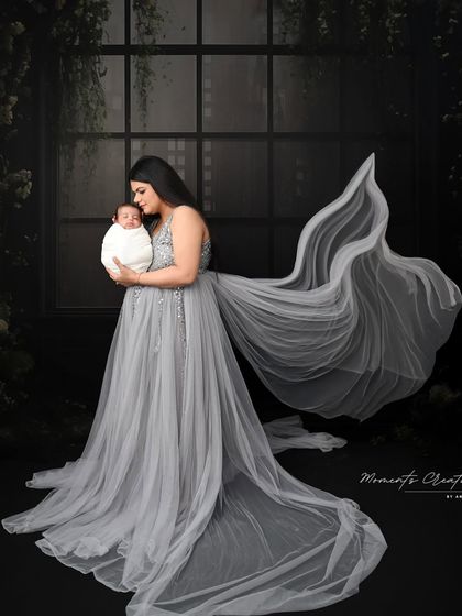 A majestic portrait of a mother and her newborn. The flowing grey gown and dark, moody backdrop create a dramatic and elegant image that feels like a classic painting.