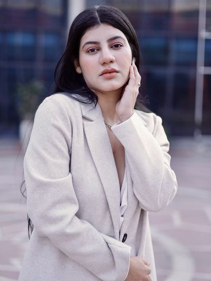 A close-up portrait against a modern architectural background, highlighting the model's serene expression and the texture of her coat.