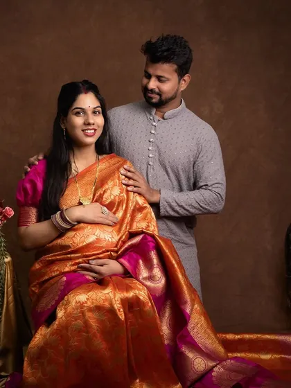 Seated gracefully, this mother to be looks radiant in her orange and pink saree. This studio setup allows for classic, poised portraits that highlight the beauty and strength of pregnancy.