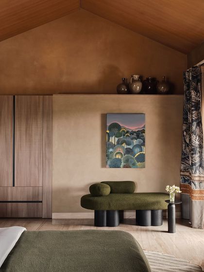 A view of a bedroom with a vaulted wooden ceiling and lime-washed walls. We used a sculptural olive green chaise and contemporary art to add character, balancing minimalism with curated, soulful pieces.